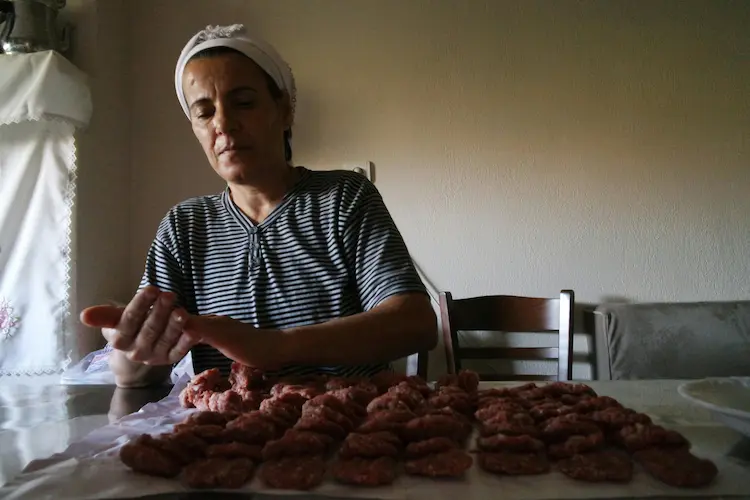 Grandma is rolling meatballs at a table wearing a striped shirt