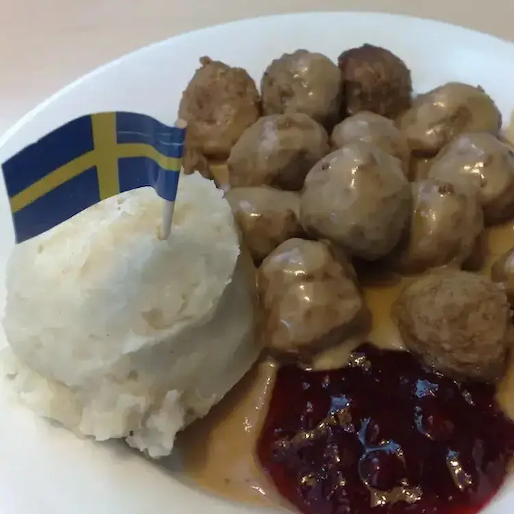 Swedish meatball dish plated with gravy, mashed potatoes, cranberries and garnished with a Swedish flag