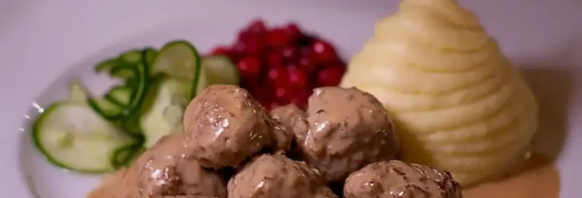 Plate of swedish meatballs with mashed potatoes, gravy, pickled cucumber salad and cranberries