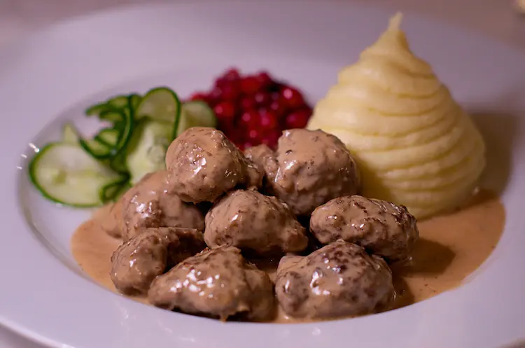 A plate of Swedish meatballs with mashed potatoes, gravy, pickled cucumber salad and cranberries